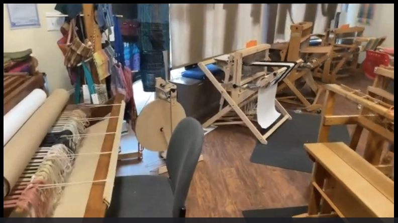 A room filled with weaving looms, weaving projects, and a spinning wheel