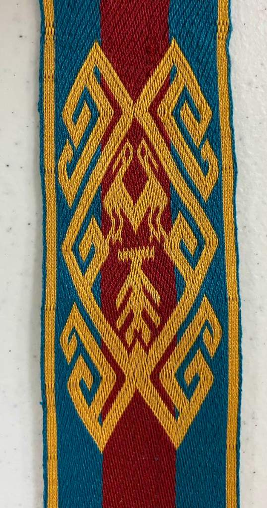 David W. - Detail of a tablet woven band of two gold birds surrounded by a gold motif on a blue and red striped background.