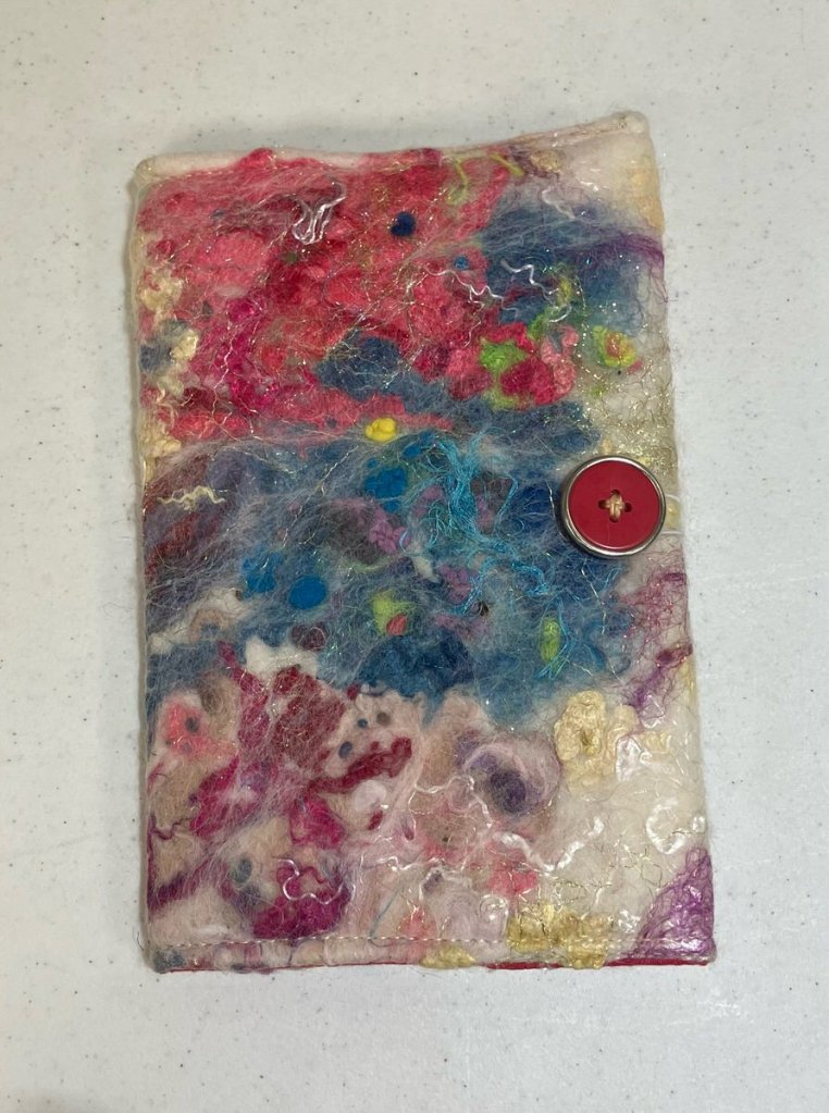 Multicolored felt, threads, and strings felted onto a white background with a red button.