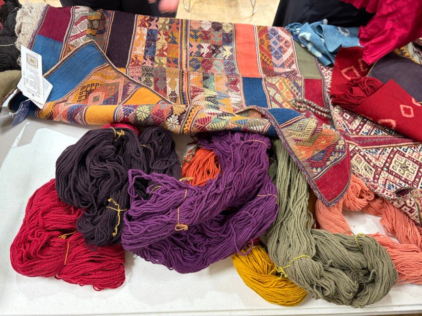 Several woven and dyed textiles on a table along with several skeins of brightly dyed wool.