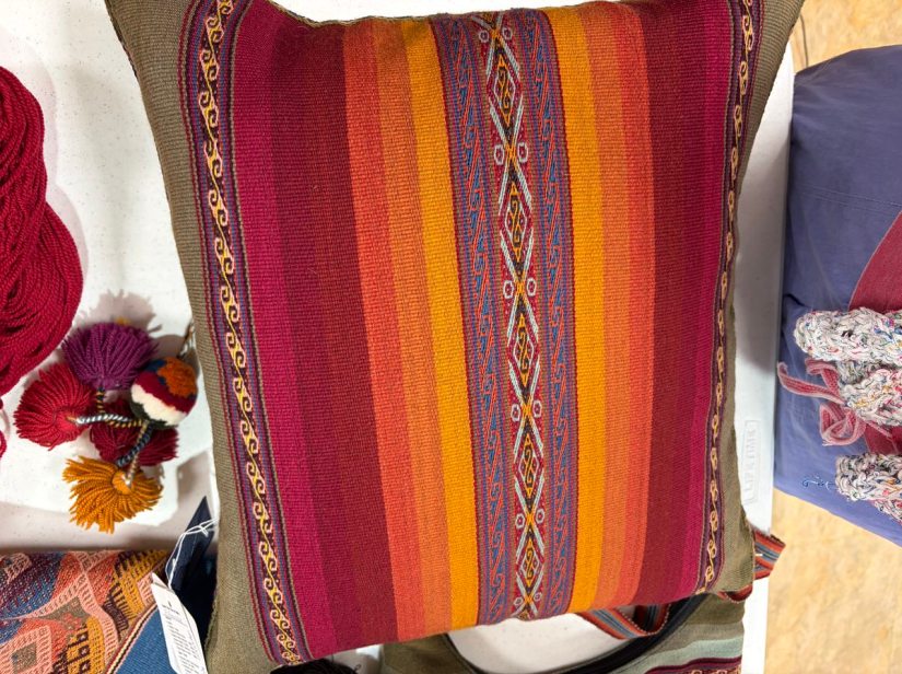 A woven pillow with multiple bright-colored plain stripes and intricately woven stripes in shades of tan, red, pink, yellow, and orange.