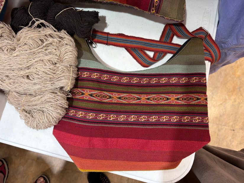 A handwoven purse and handspun yarn. The purse incorporates sever stripes that are plan and patterned in shades of green, red, orange and yellow.