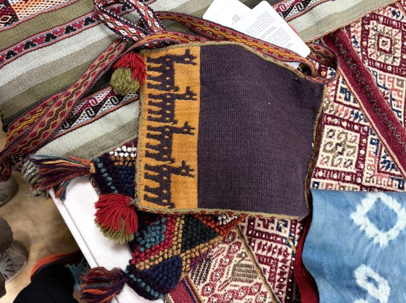 A small handwoven shoulder bag with four woven alpacas along the bottom edge; the bag is woven in shades of deep brown and gold, with a patterned strap.