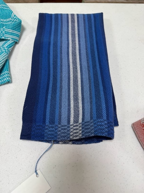 A blue, gray, and white vertically striped twill towel on a table.