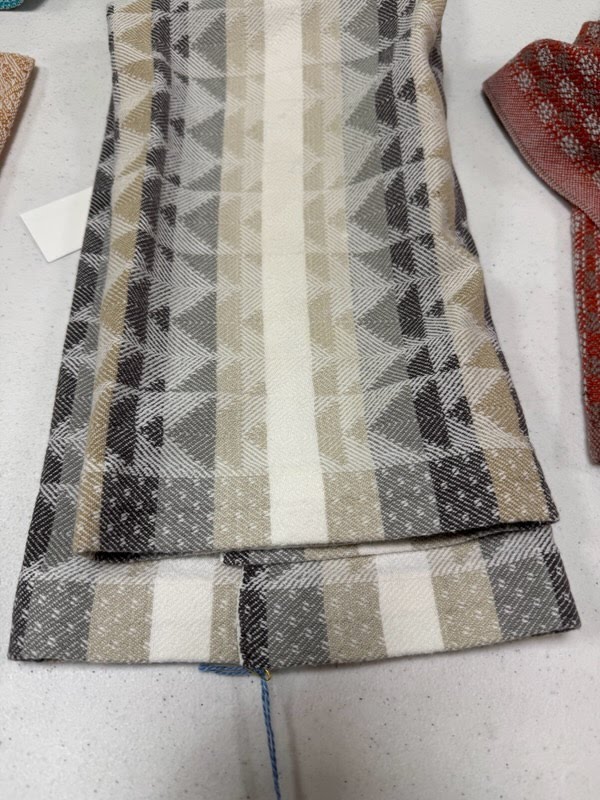 A handwoven towel in shades of tan, cream, and gray on a table.