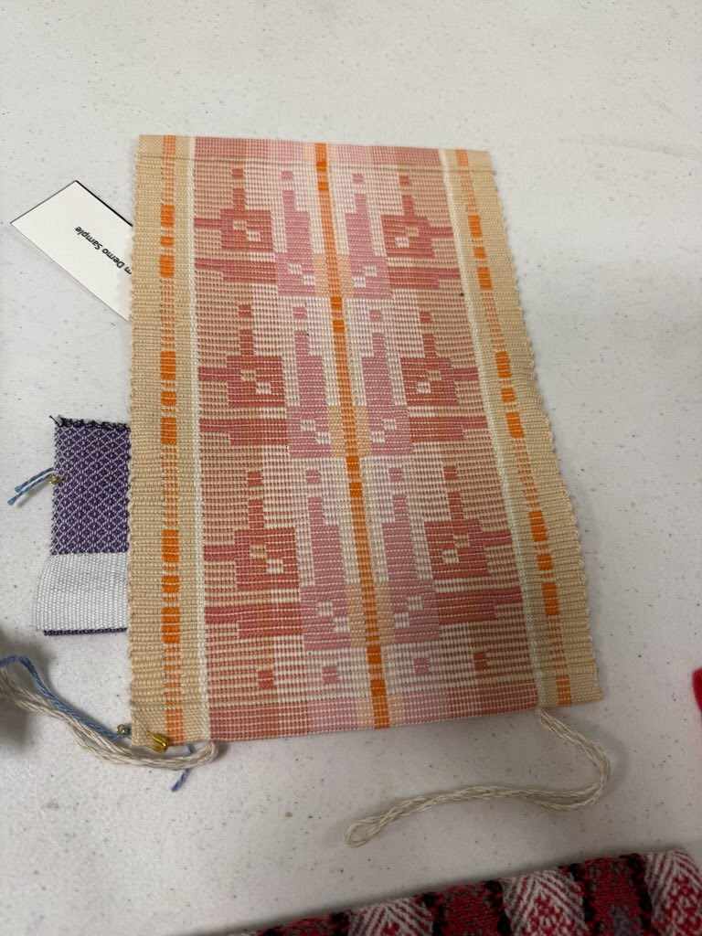 A handwoven textile, featuring a modernistic motif, in shades of tan, orange, and cream on a table.