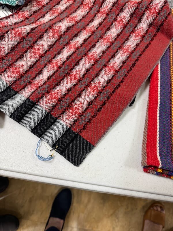 A handwoven textile in shades of red, gray, and whioe, featuring vertical stripes, on a table.
